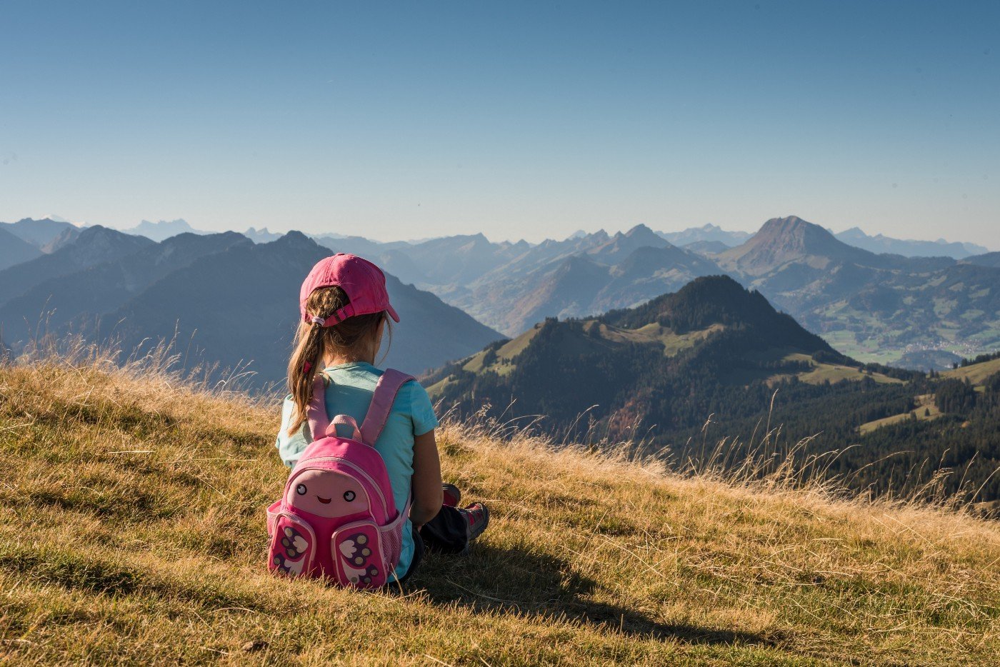 child sitting in a field looking at a mountain