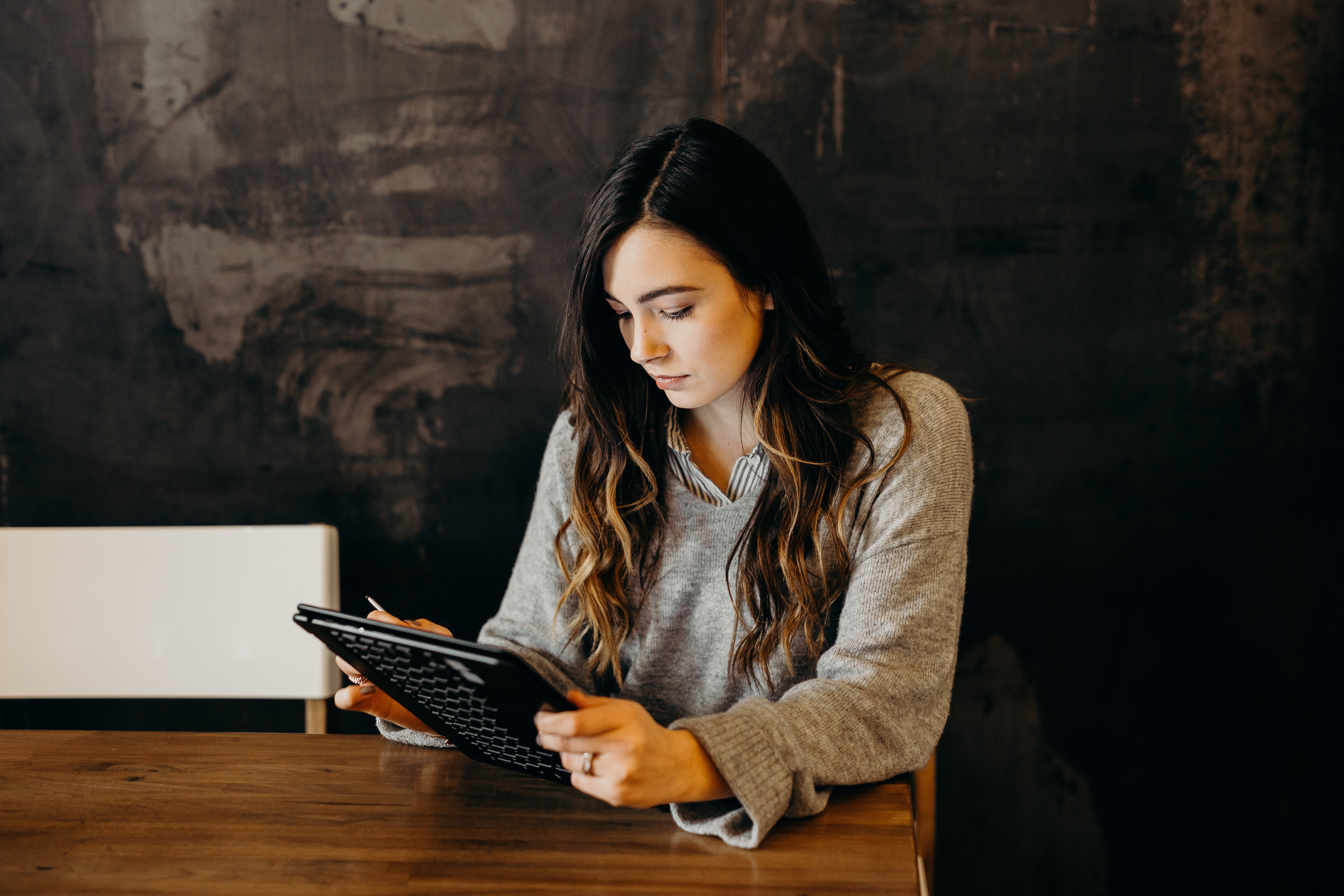 A woman sits at a table looking down at an e-tablet.